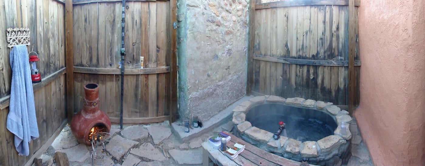 Sala fechada com portas de madeira e banheira de água termal em pedra.