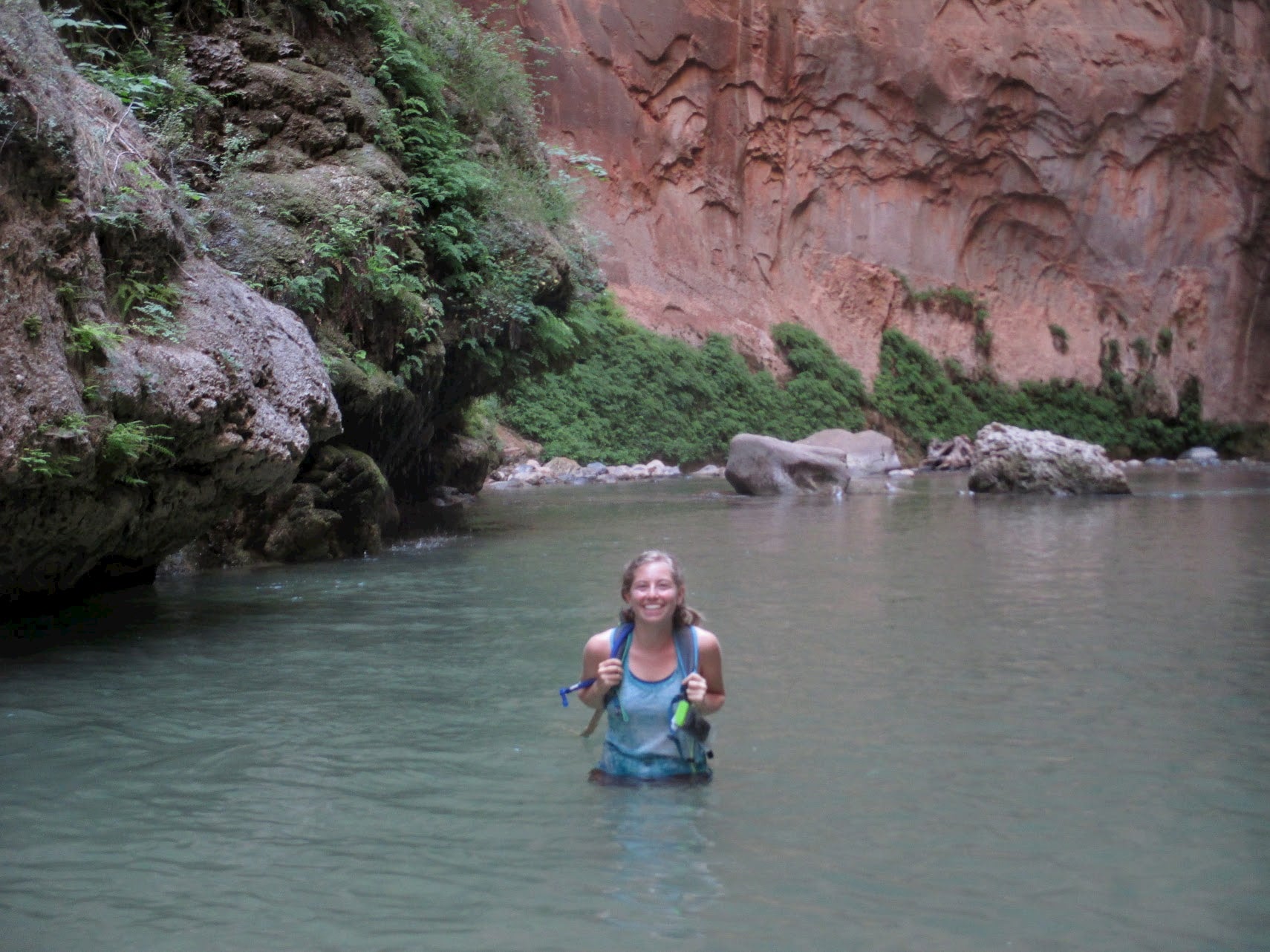 Women with backpack wading through water in a canyon.