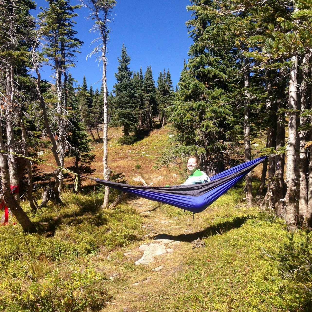 Women peeping out of hammock between two trees in the backcountry.