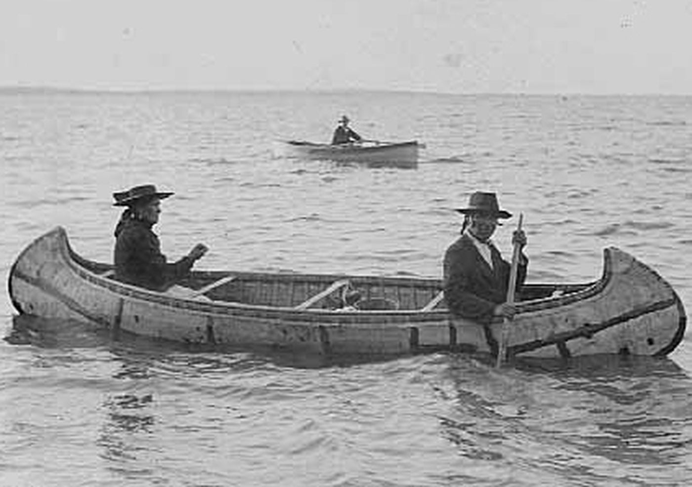 Antique image of Native Americans sharing a canoe in open water.