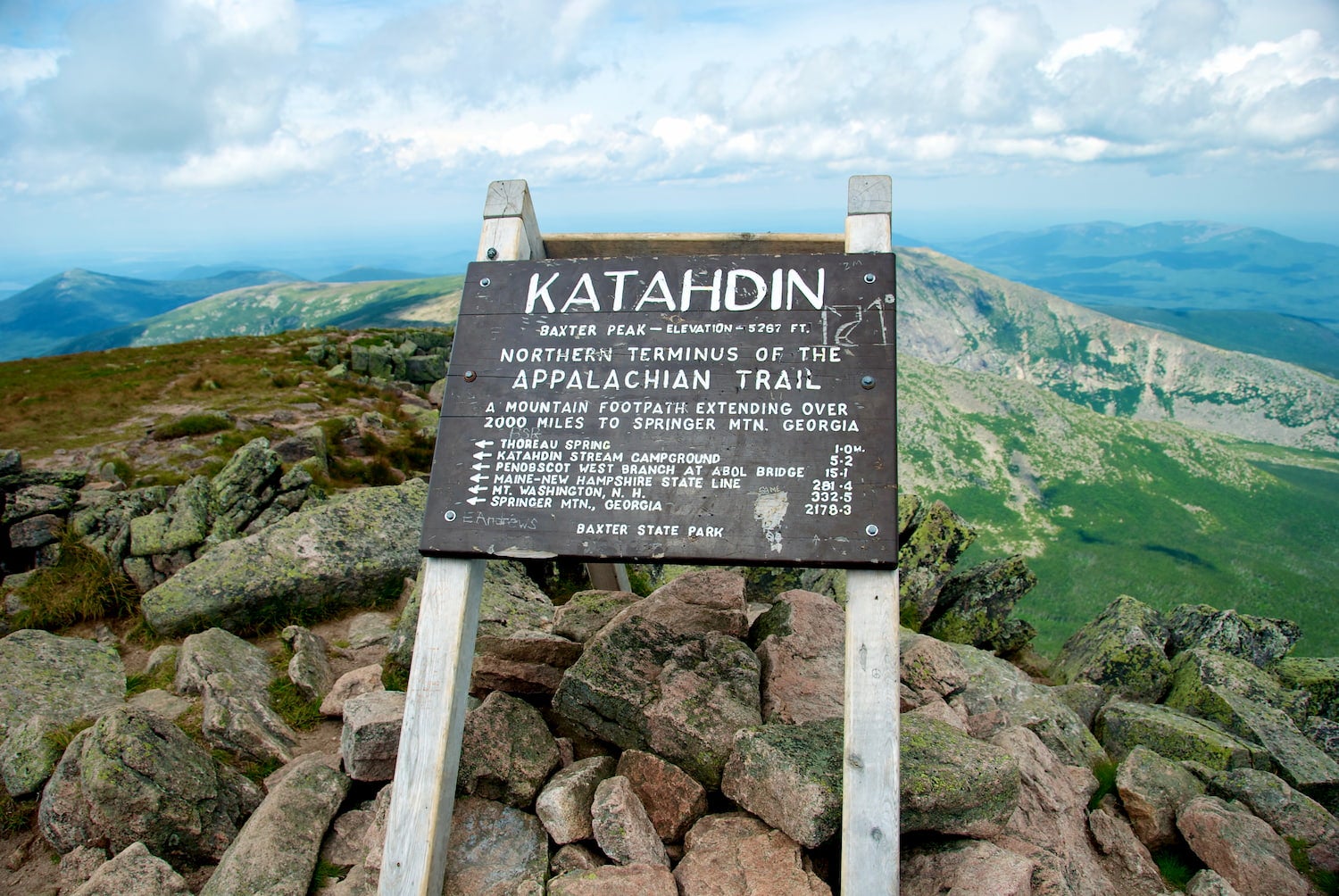 "Kathadin" sign on top of mountain surrounding by green alpine landscape.