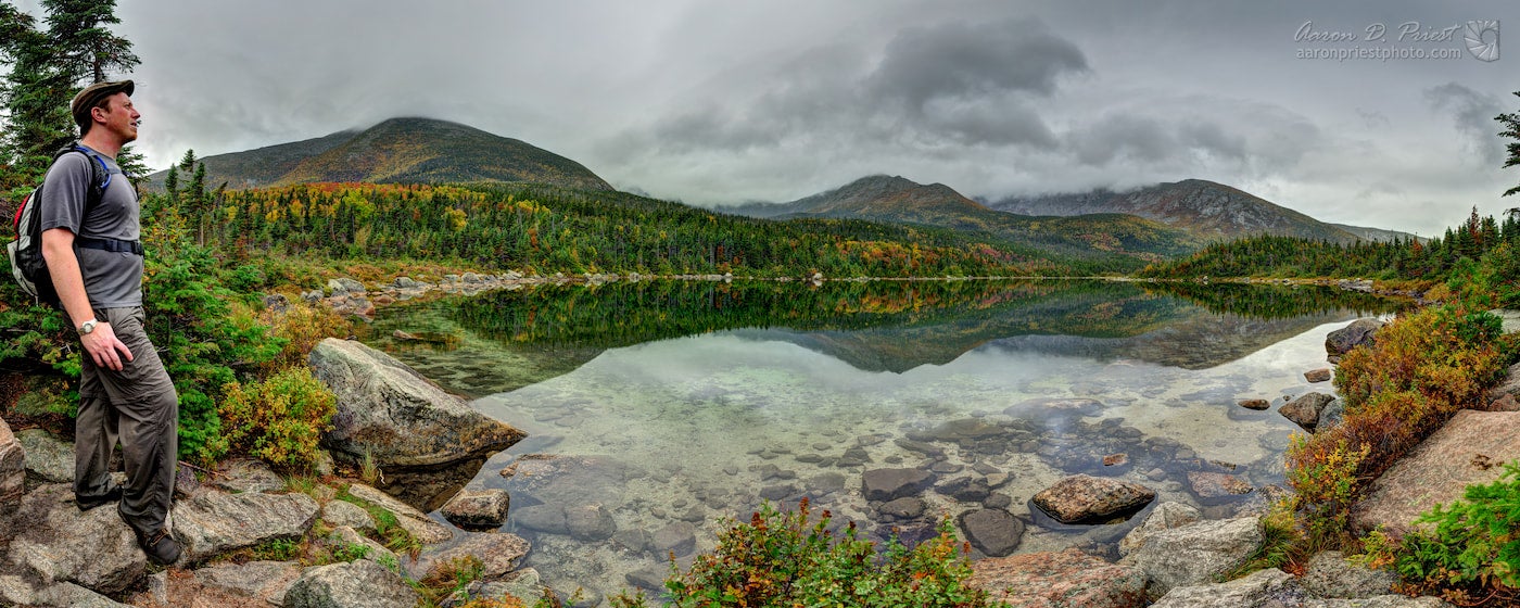 Hiker beside lake with mountains in the background.