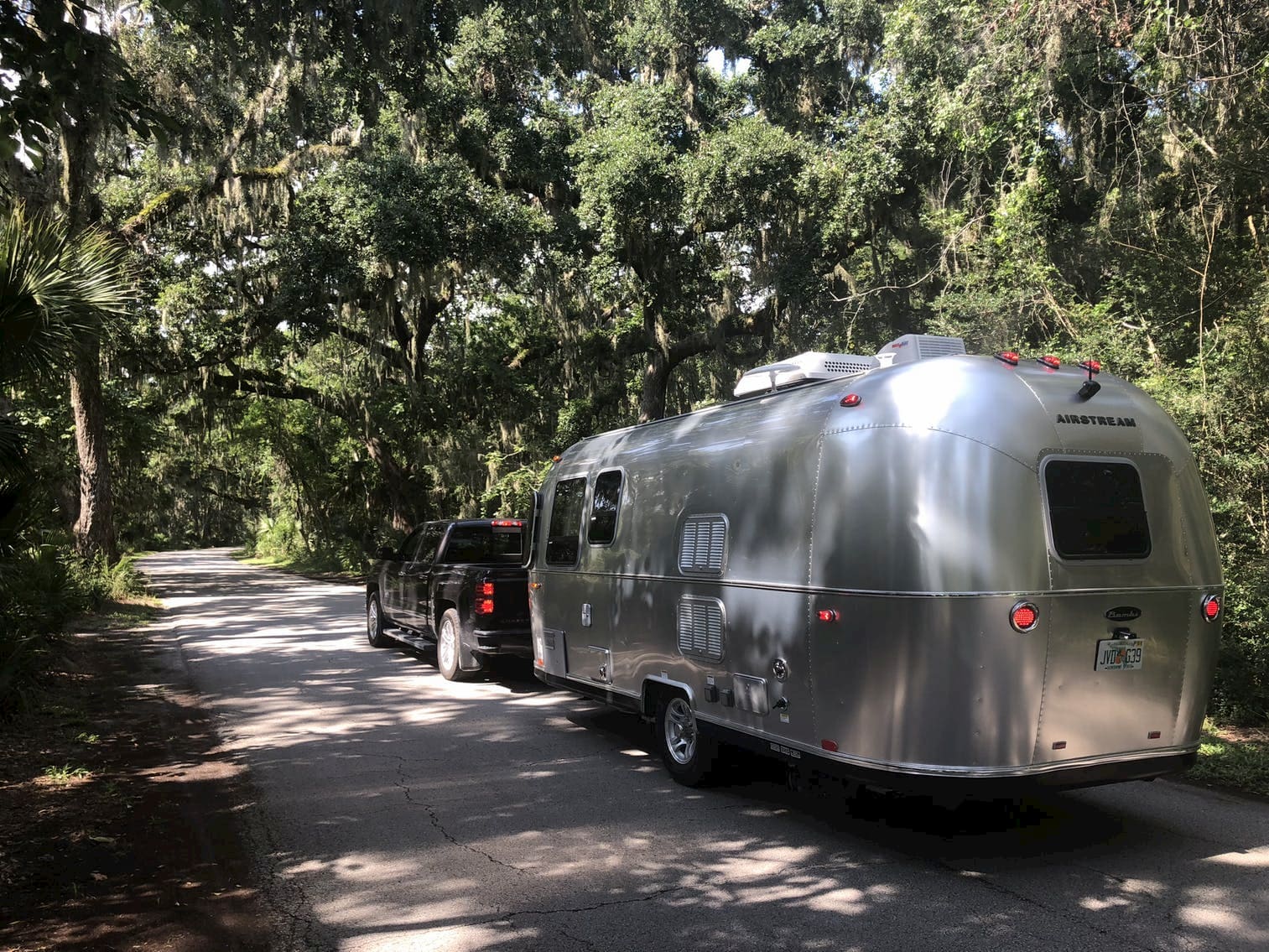 Pickup truck pulling airstream trailer on a road through a tropical forest.