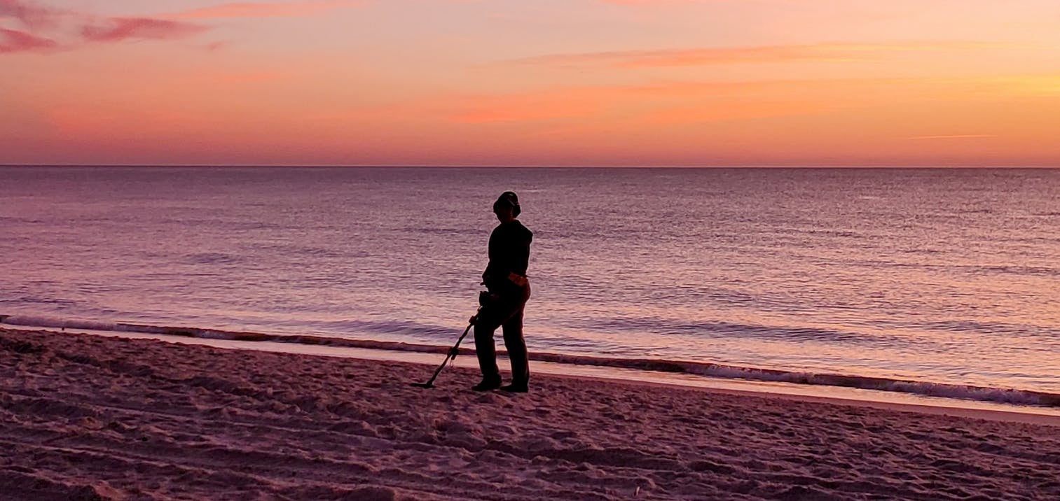 Person using metal detector during sunset on the beach.