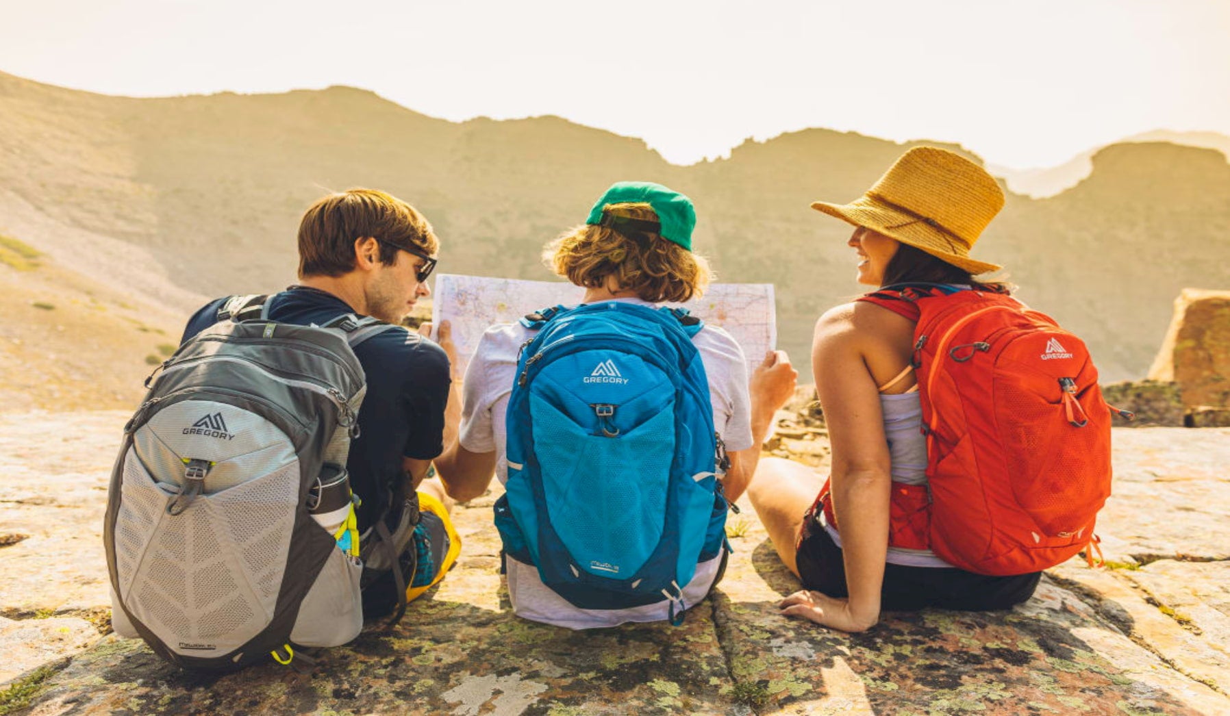 Two kids and their mom wearing gregory backpacks looking at a map in an alpine landscape.