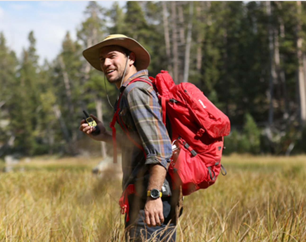 Man hiking with hat, backpack, and walkie talkie.