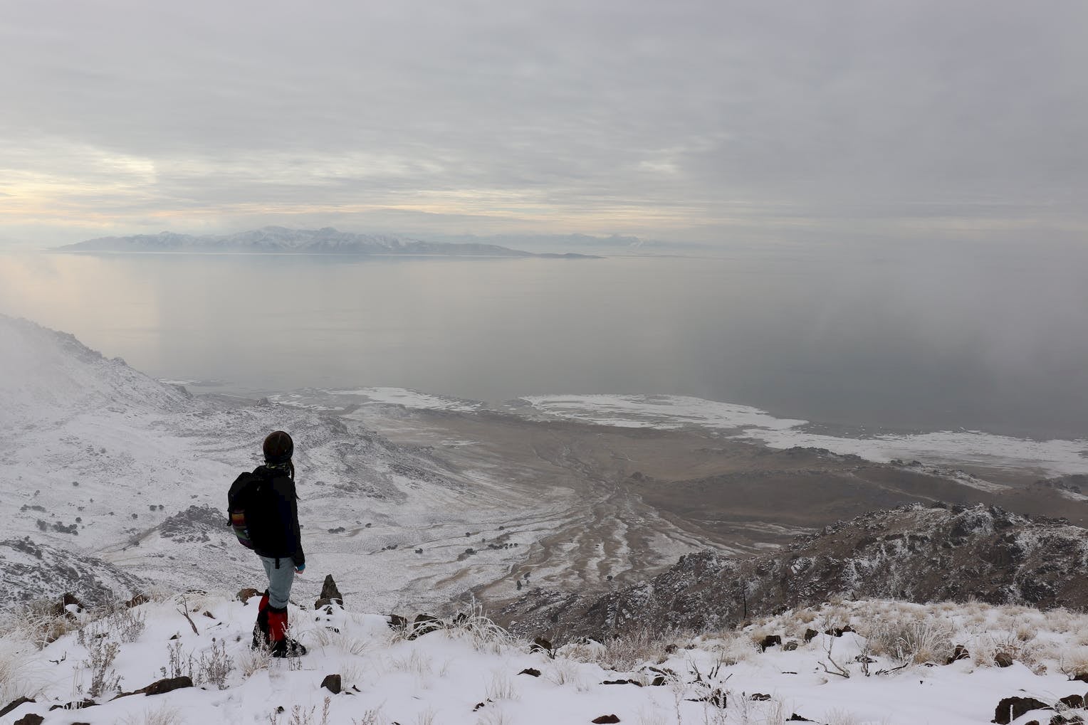 Hiker in gaiters and winter clothes overlooking snow dusted island from a hilltop.