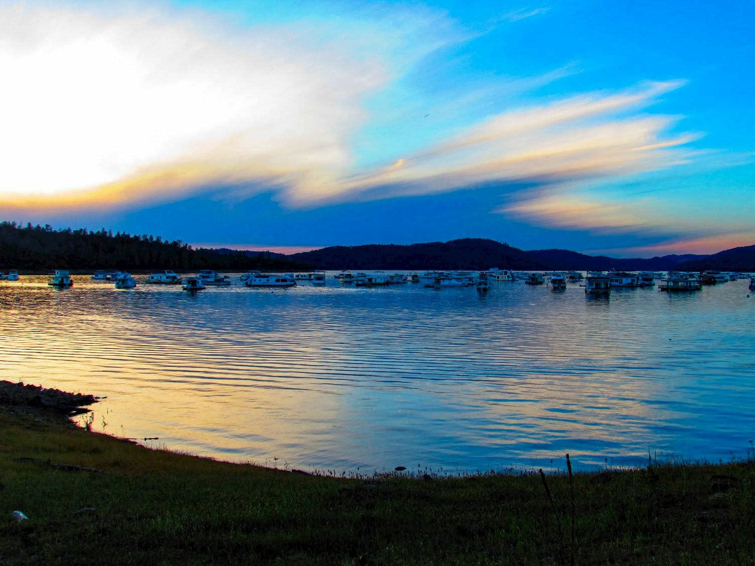 Sunset and colorful clouds over a lake where boats are anchored.