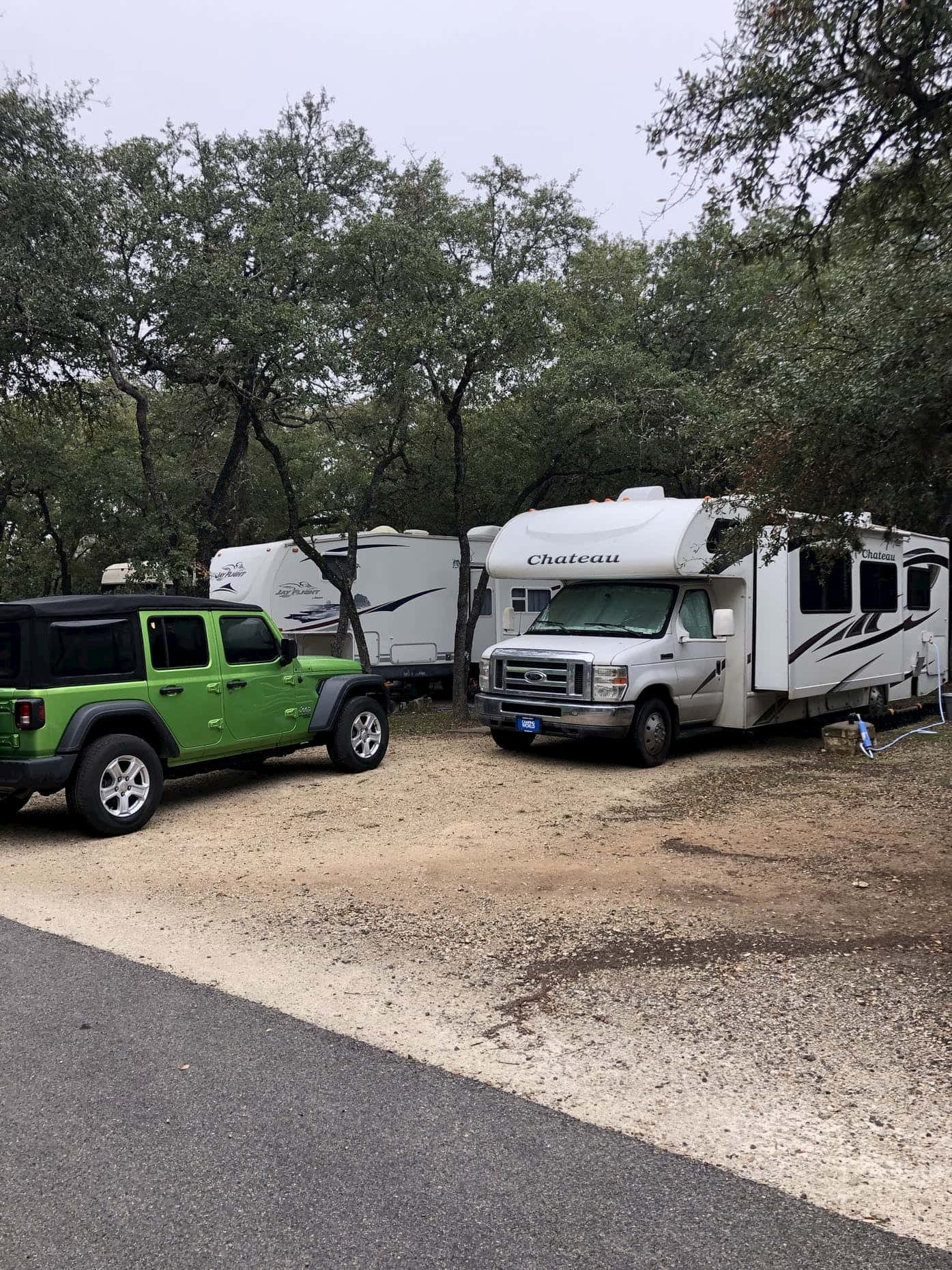 Two RVs parked beside a green jeep in a gravel campsite.