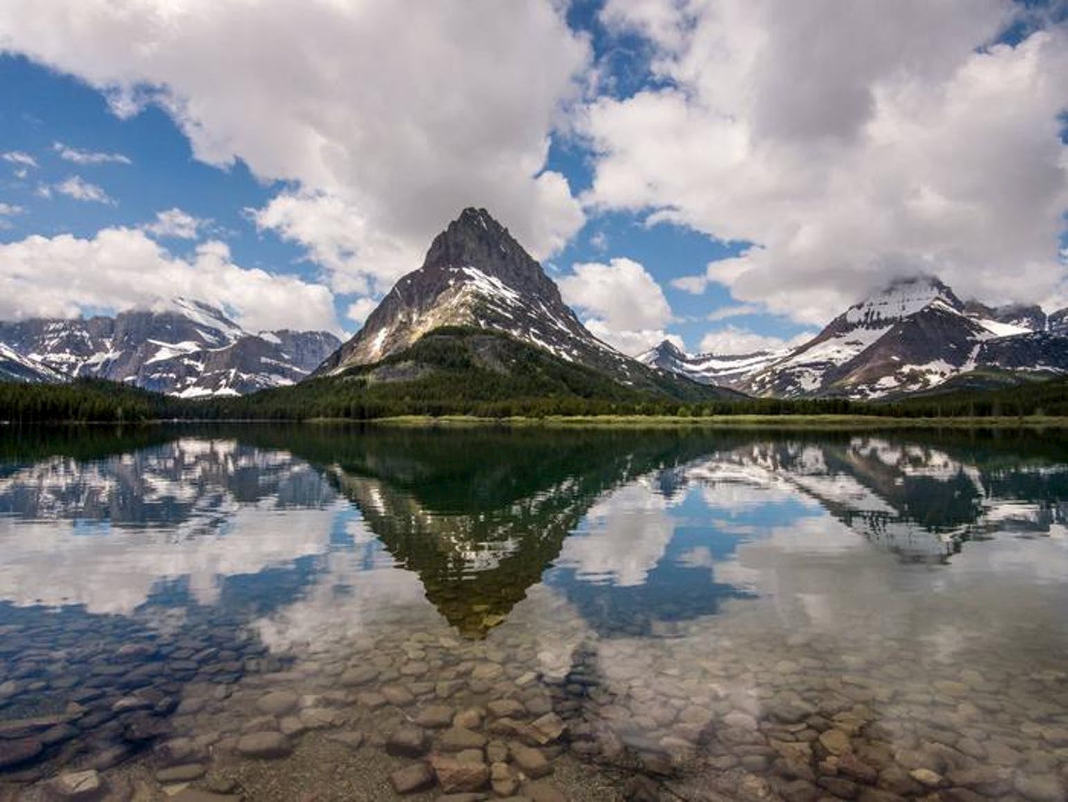 Landscape of mountains dotted with snows and their reflection in the lake below.