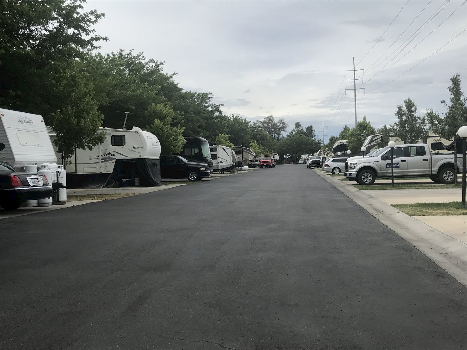 A stretch of road in an RV park lined with RVs and a green lawn.