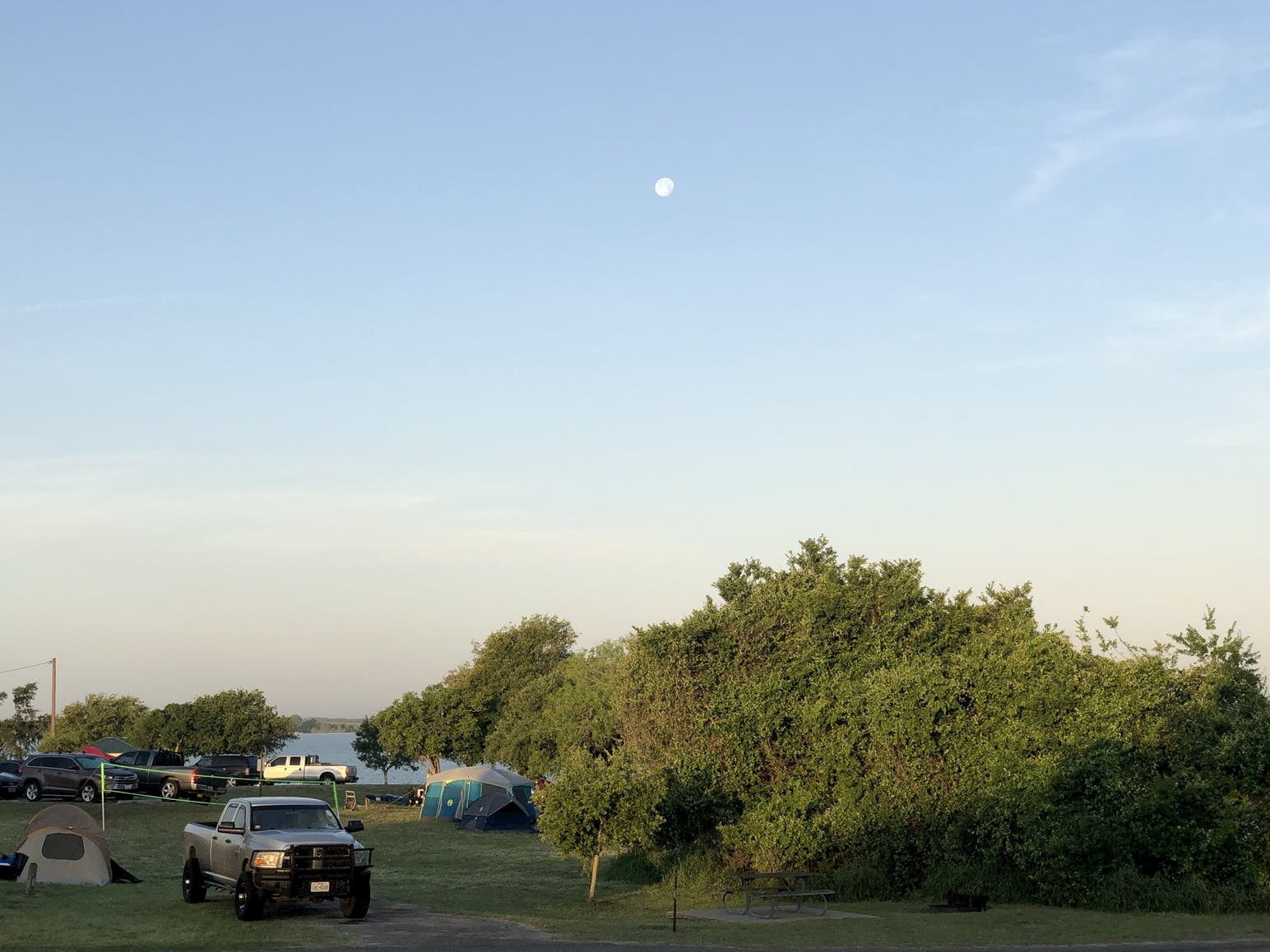 Cars parked beside tents at campground under a full moon.