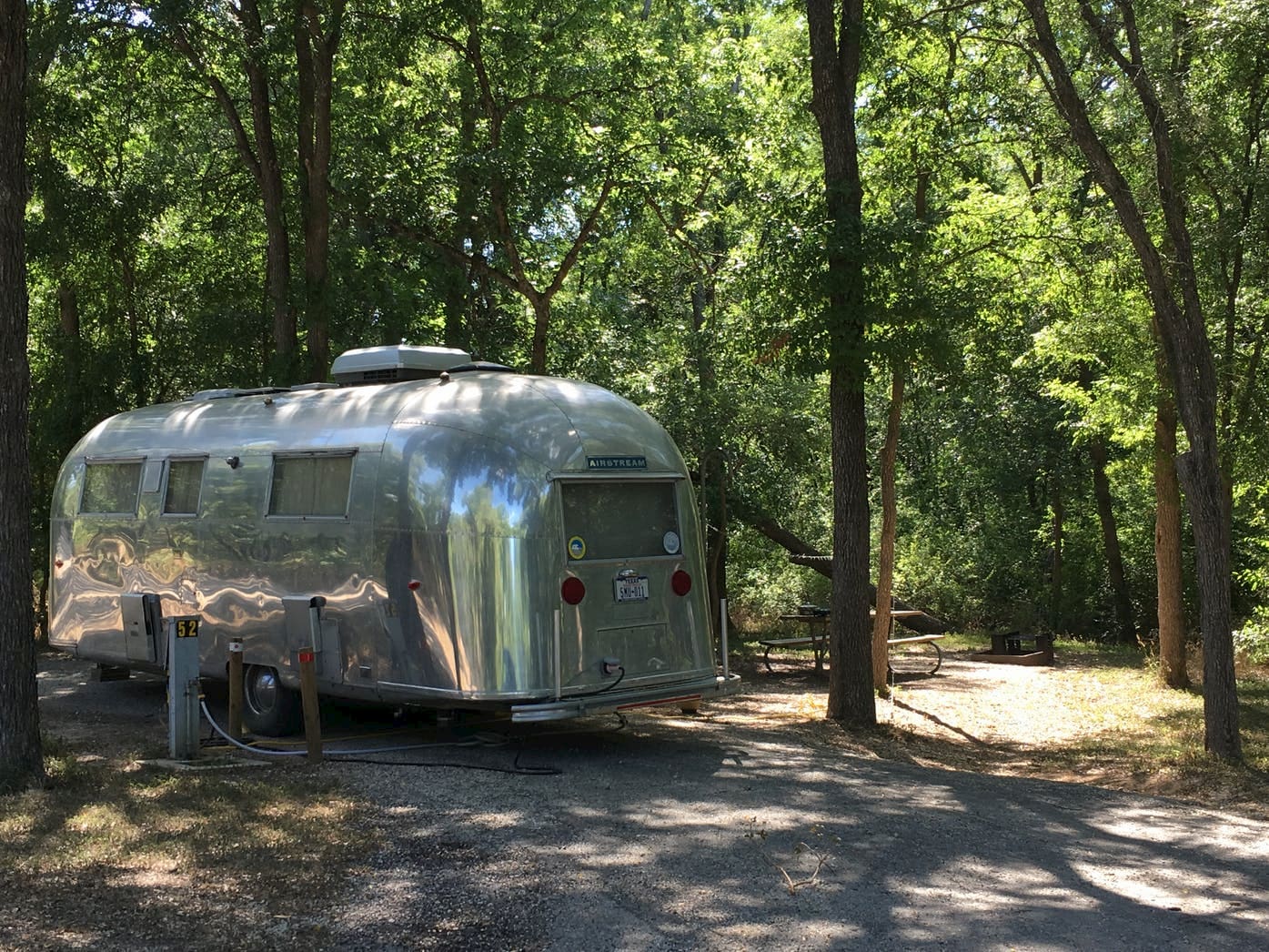 Silver airstream camper parked in wooded campsite.