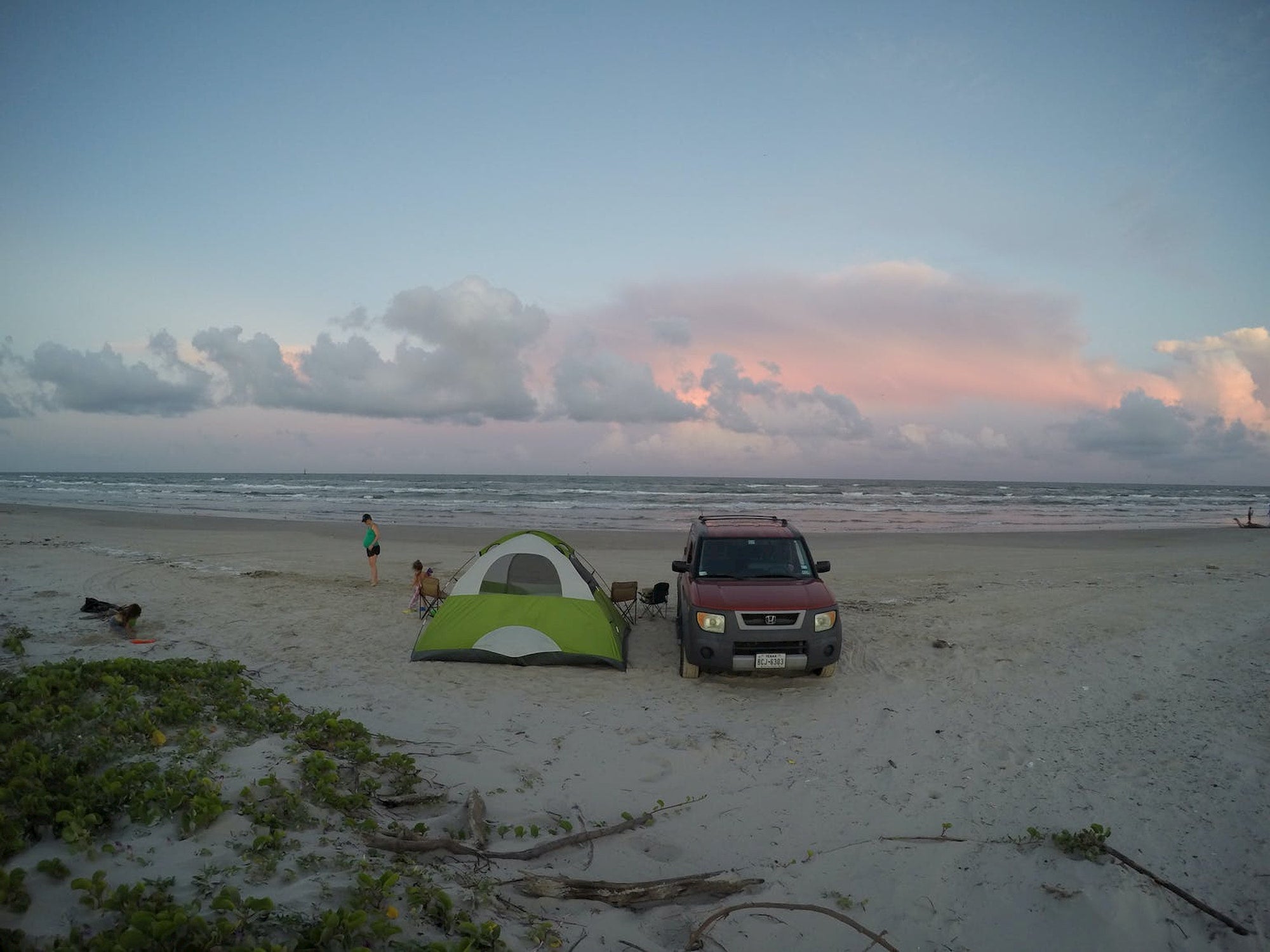 Tent set up beside car on the beach at sunset.