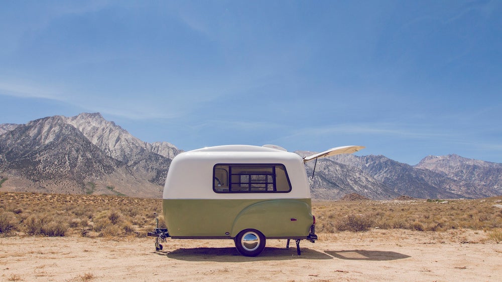 Green and white vintage camper with mountains in background 