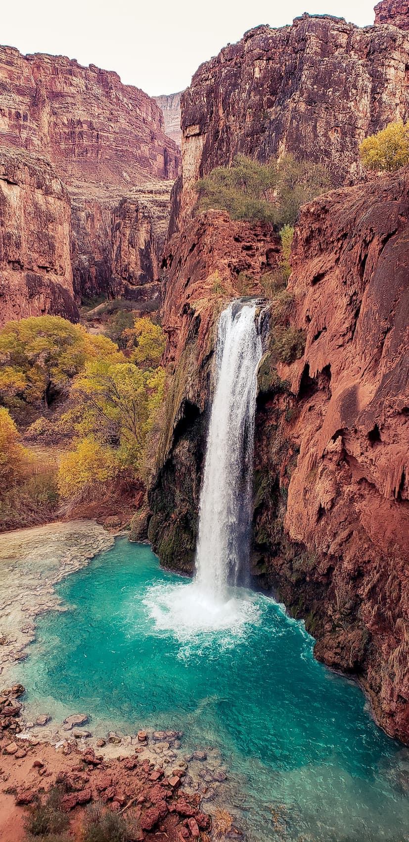 Water pouring off the top of high red rock cliffs into a bright aqua pool.