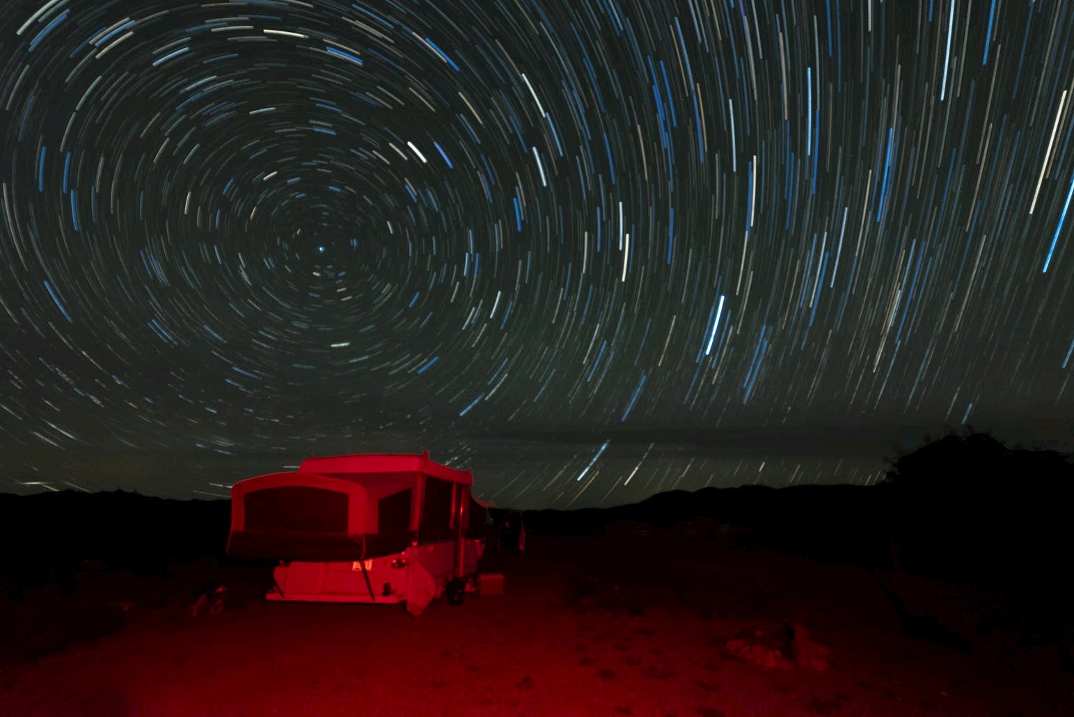 Image of stars in motion behind the a trailer illuminated in red light.