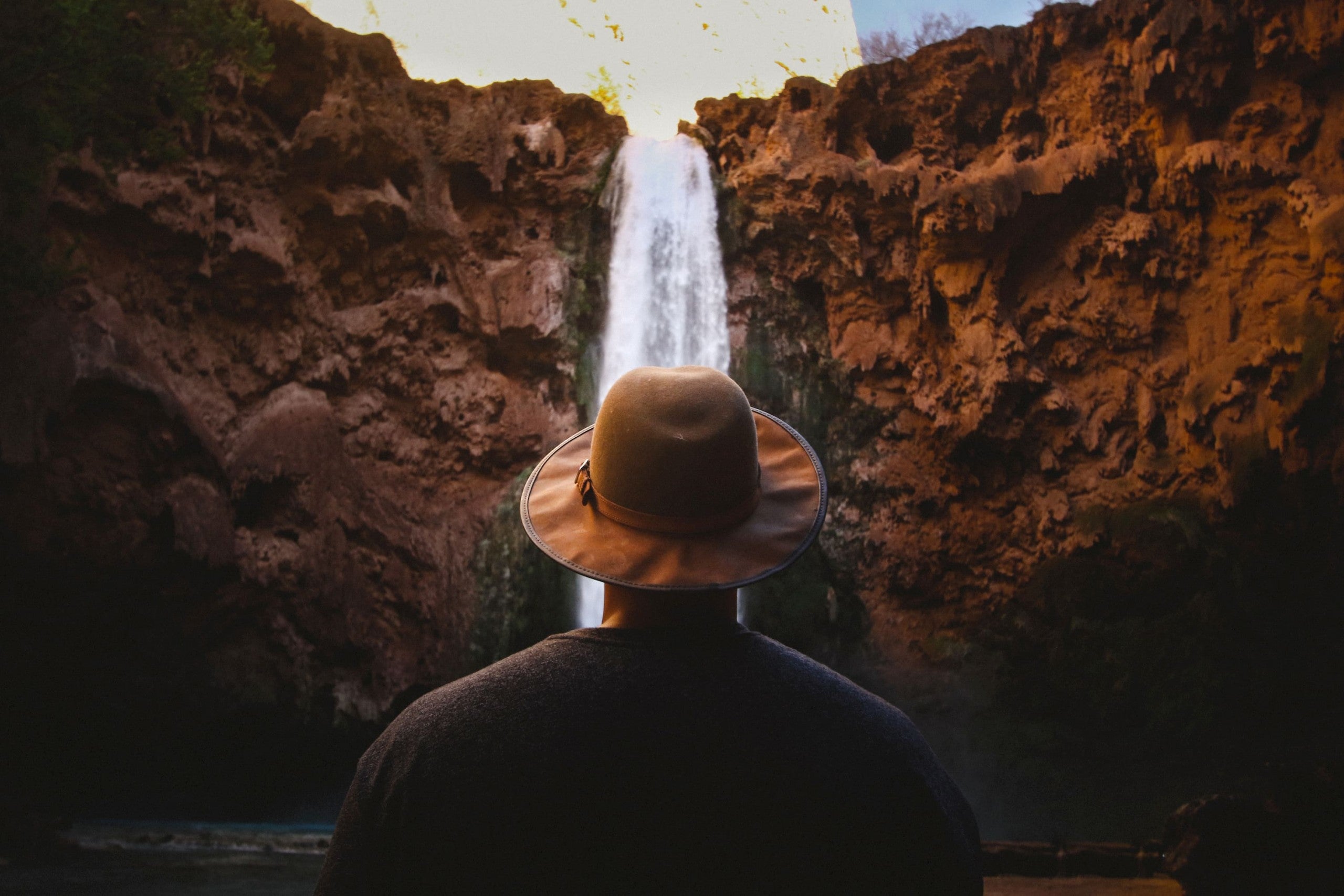 Man with hat standing in front of cascading waterfall.