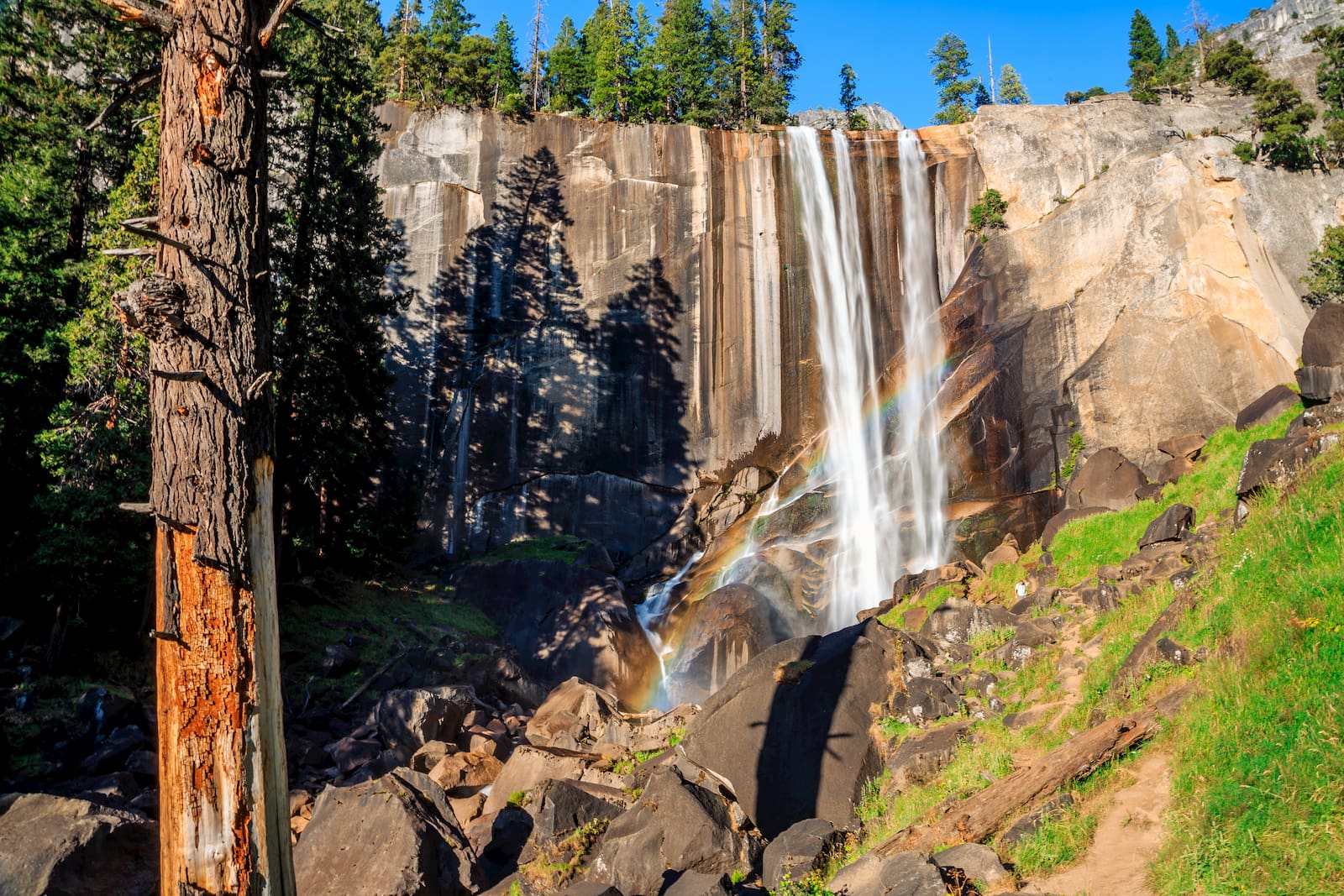 rainbow shimmering withing a waterfall crashing onto rocks below.