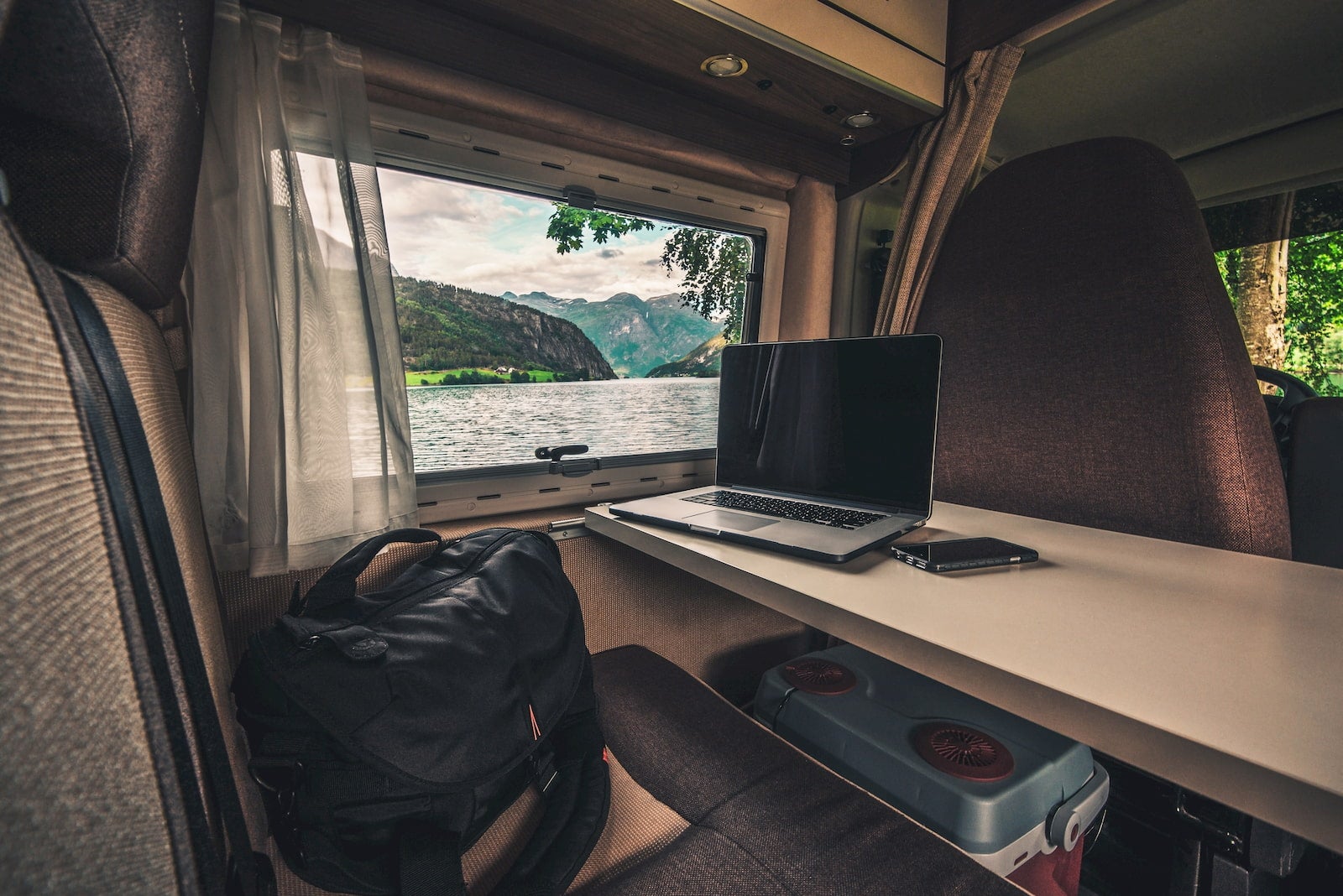 Laptop set up on RV table, beside a winndow showing a lake below mountains.