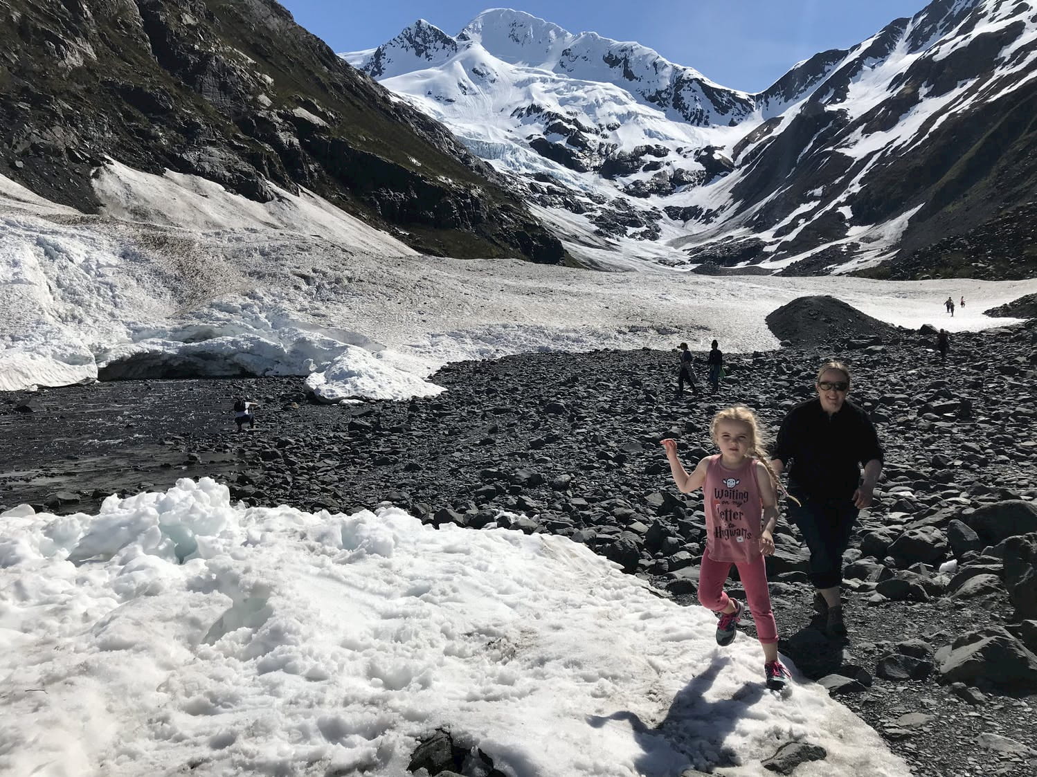 Family walking upon glacier in Alaska below a snow covered mountain.