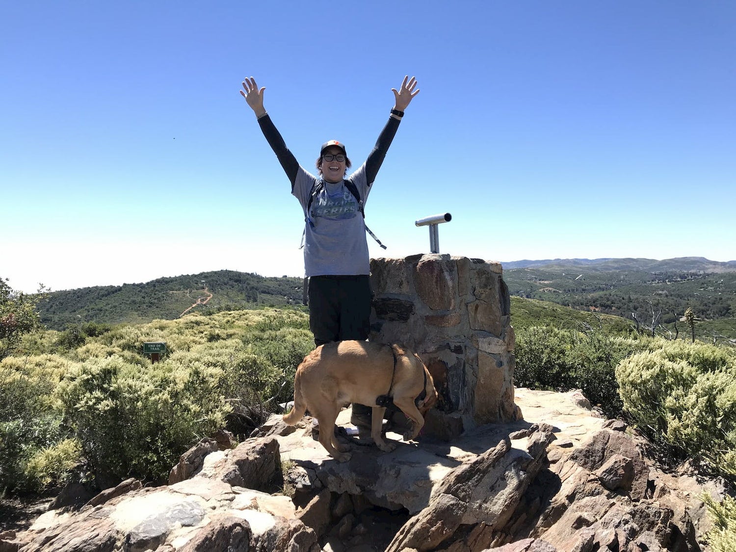person raising arms in elation with dog at their feet