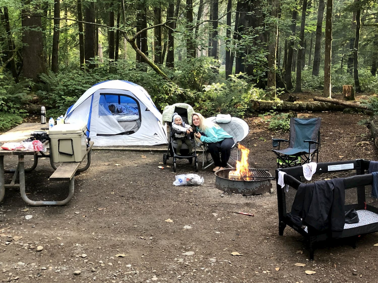 woman and baby sitting next to campfire at campsite