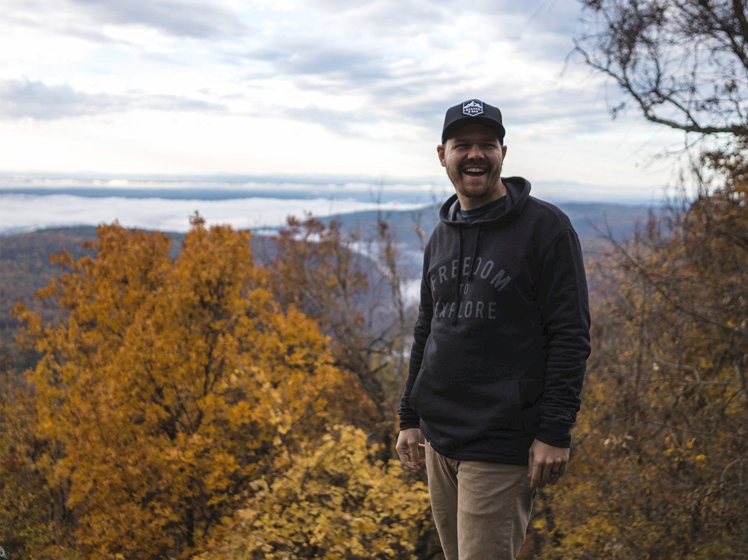 man laughing with fall colored trees behind him