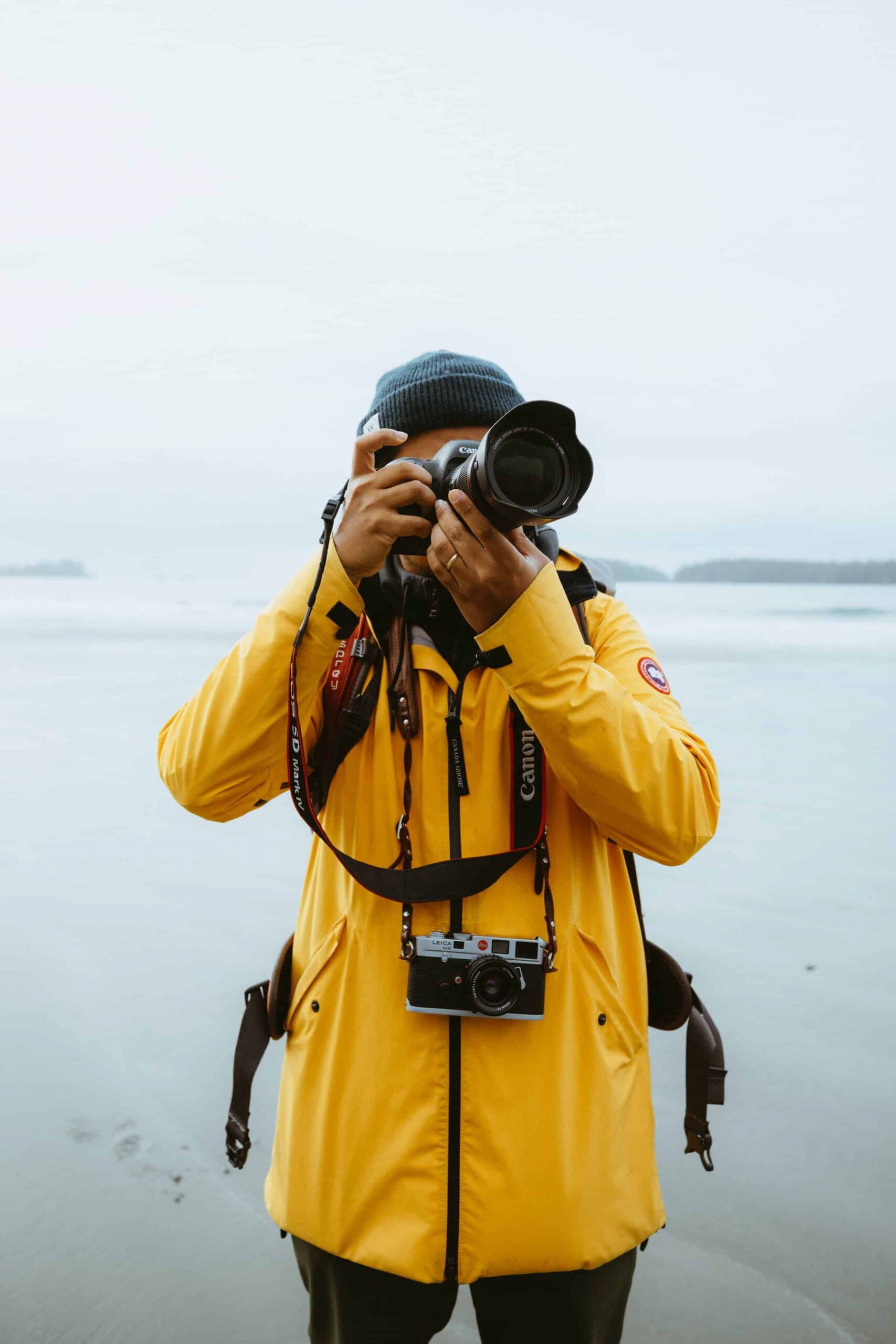 Berty Mandagie at the beach golding one camera up to his face with another hanging around his neck.