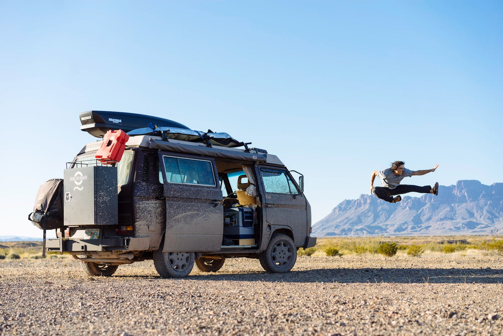 Owen from Bound for Nowhere caught in midair next to their VW Vanagon rig.