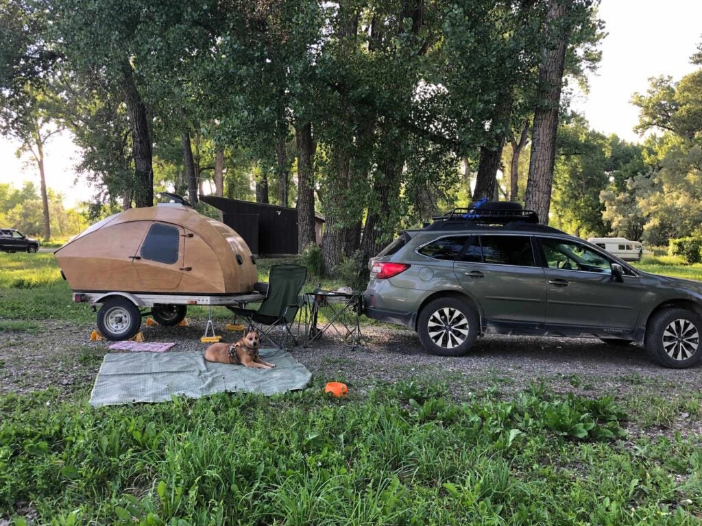 Subaru outback with wooden teardrop and blanket laid out with dog hanging out on it.