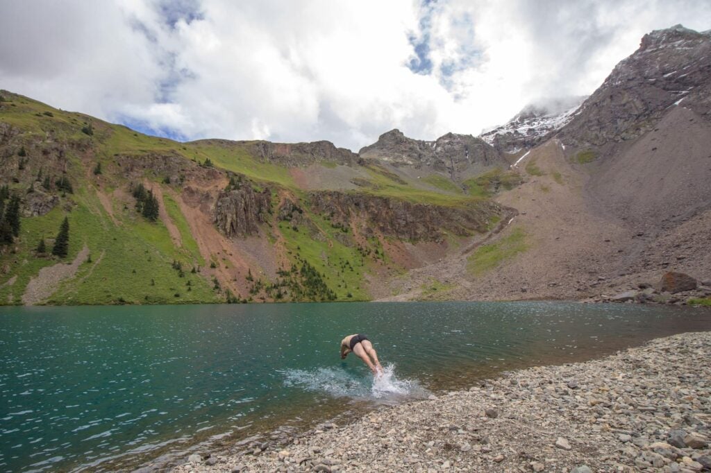 Person diving into the turquoise alpine lake below the mountains.