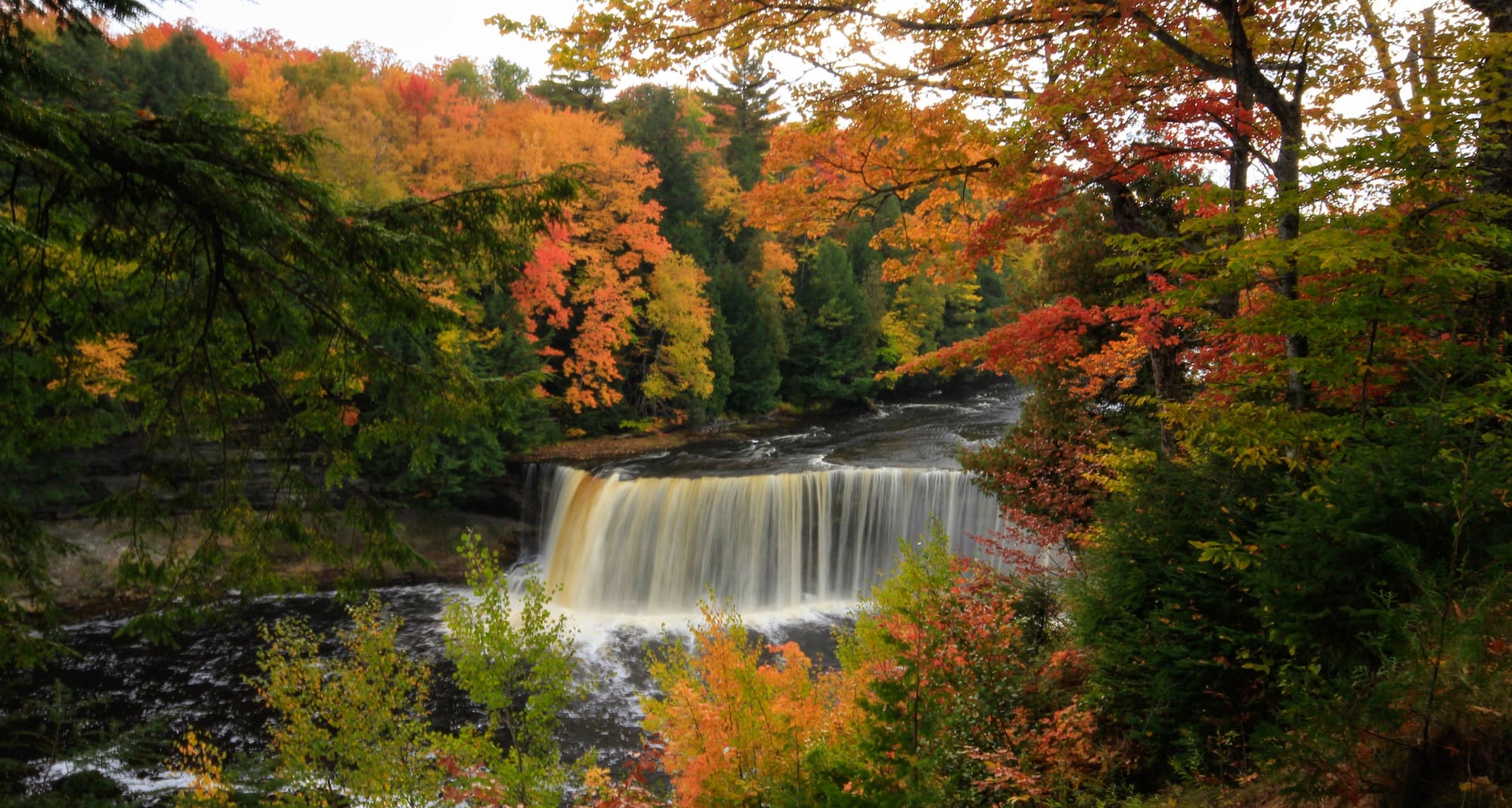 Cascading waterfalls surrounded by red and orange leaves of the fall foliage.