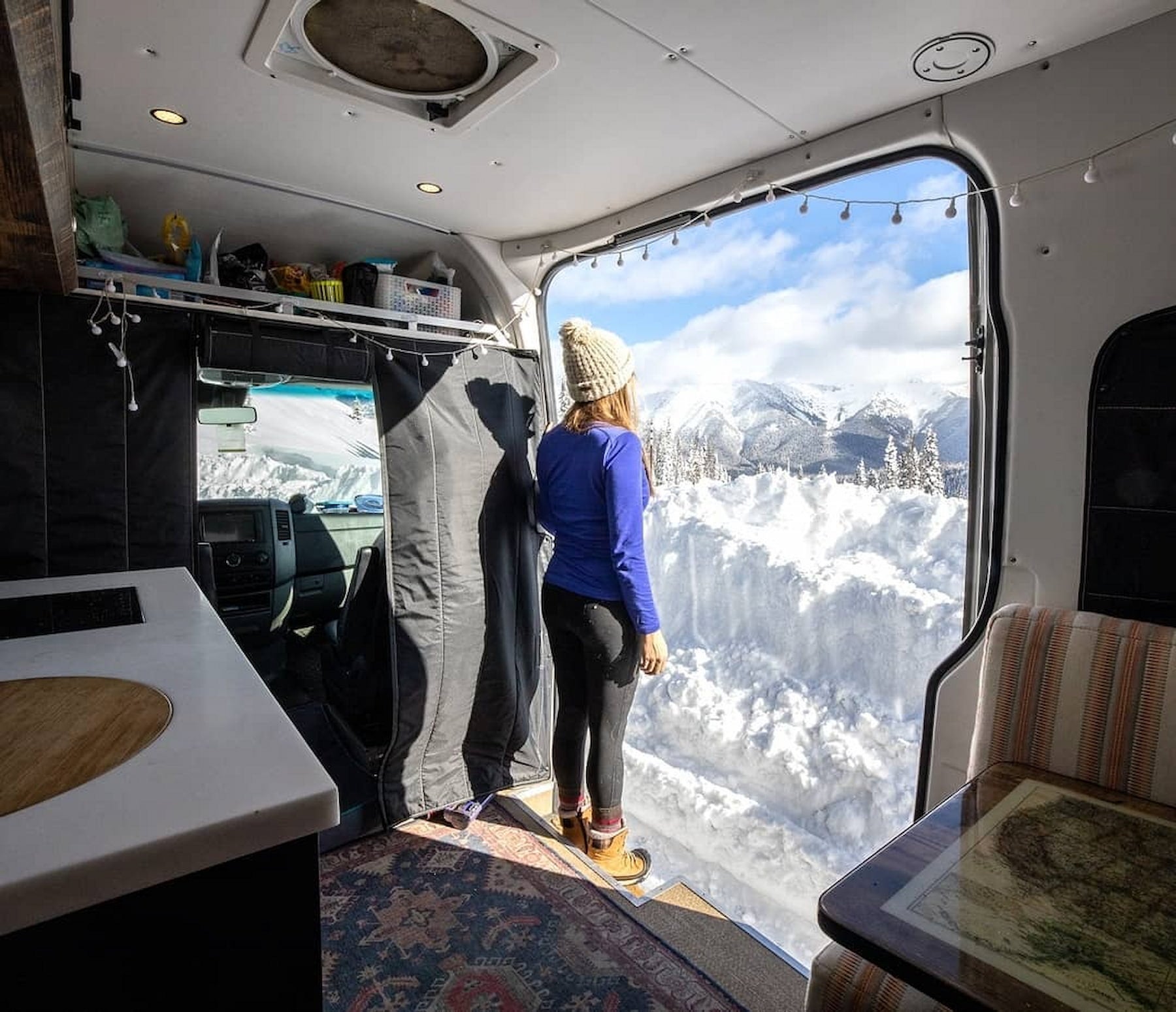 Kristin standing in the doorway of her van looking over the snow dusted mountains.