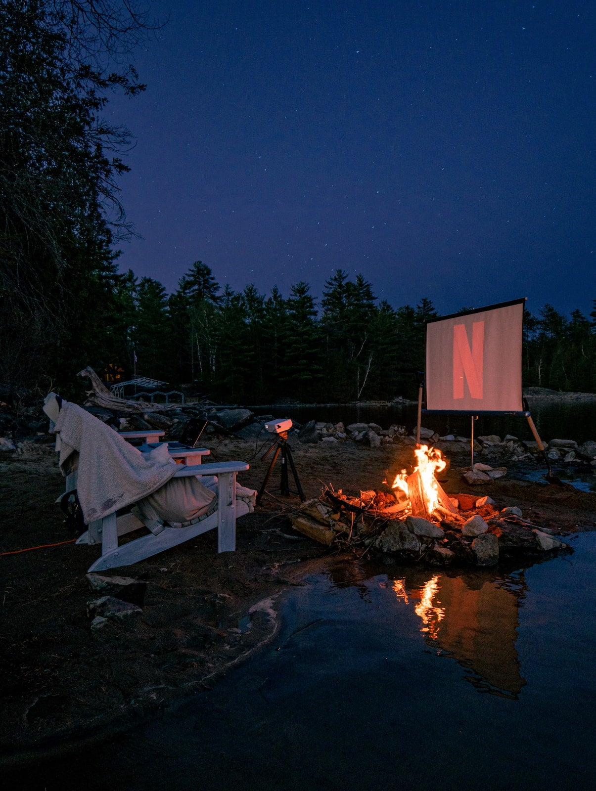 Screening a movie outside on a projector at the campsite with a campfire blazing.