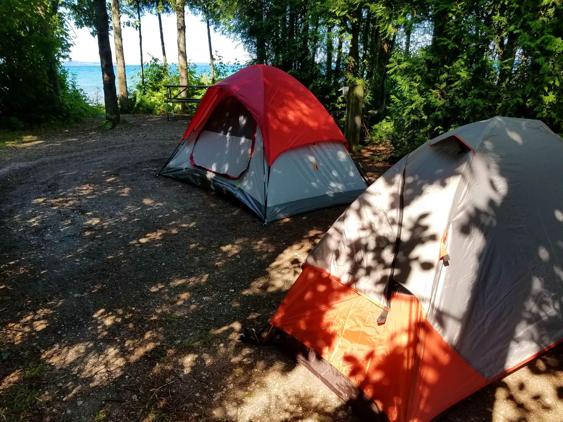 Two tents pitched in a campsite overlooking a lake in the forest.