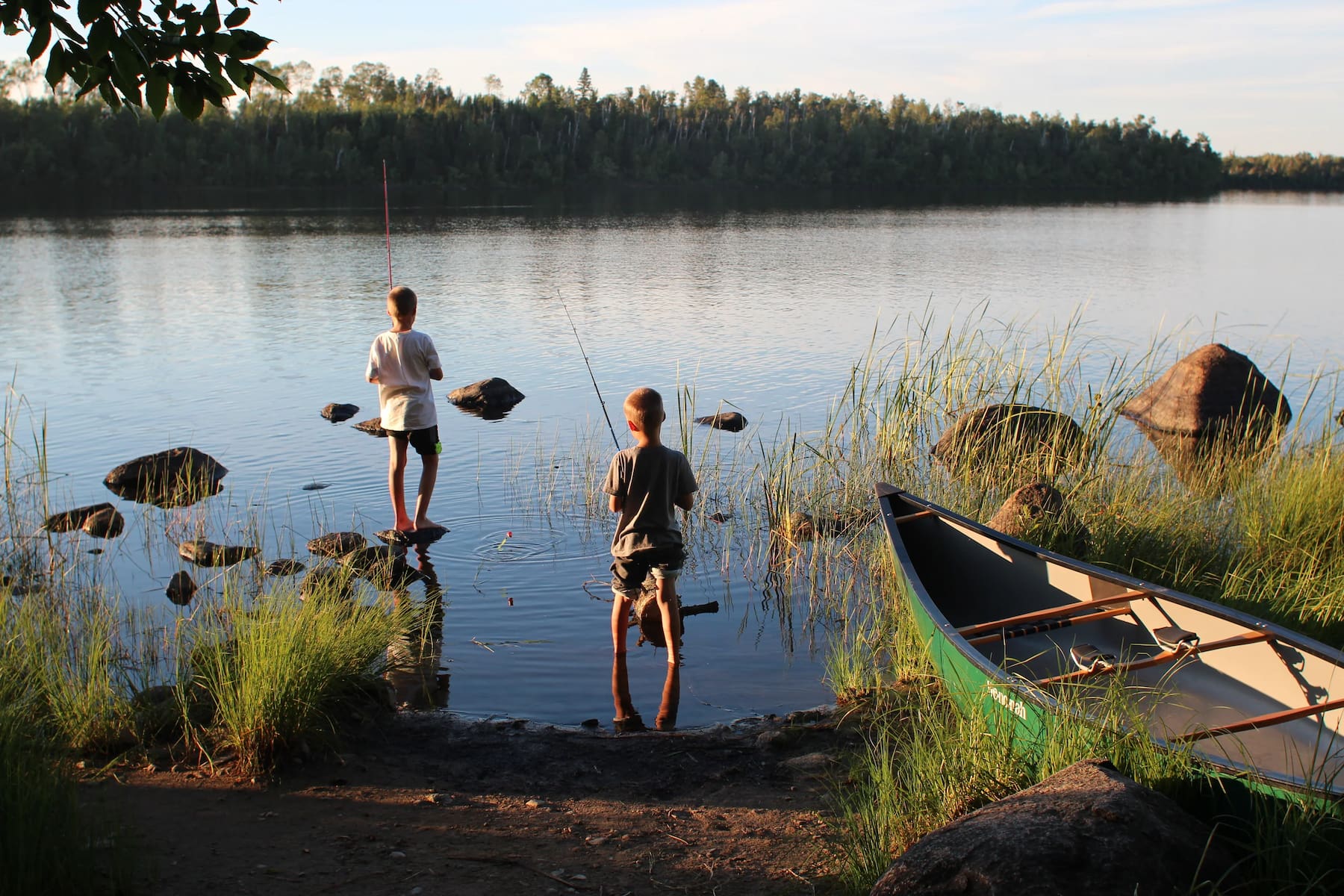 Two kids fishing beside a canoe at a waterfront campsite at Fall Lake.