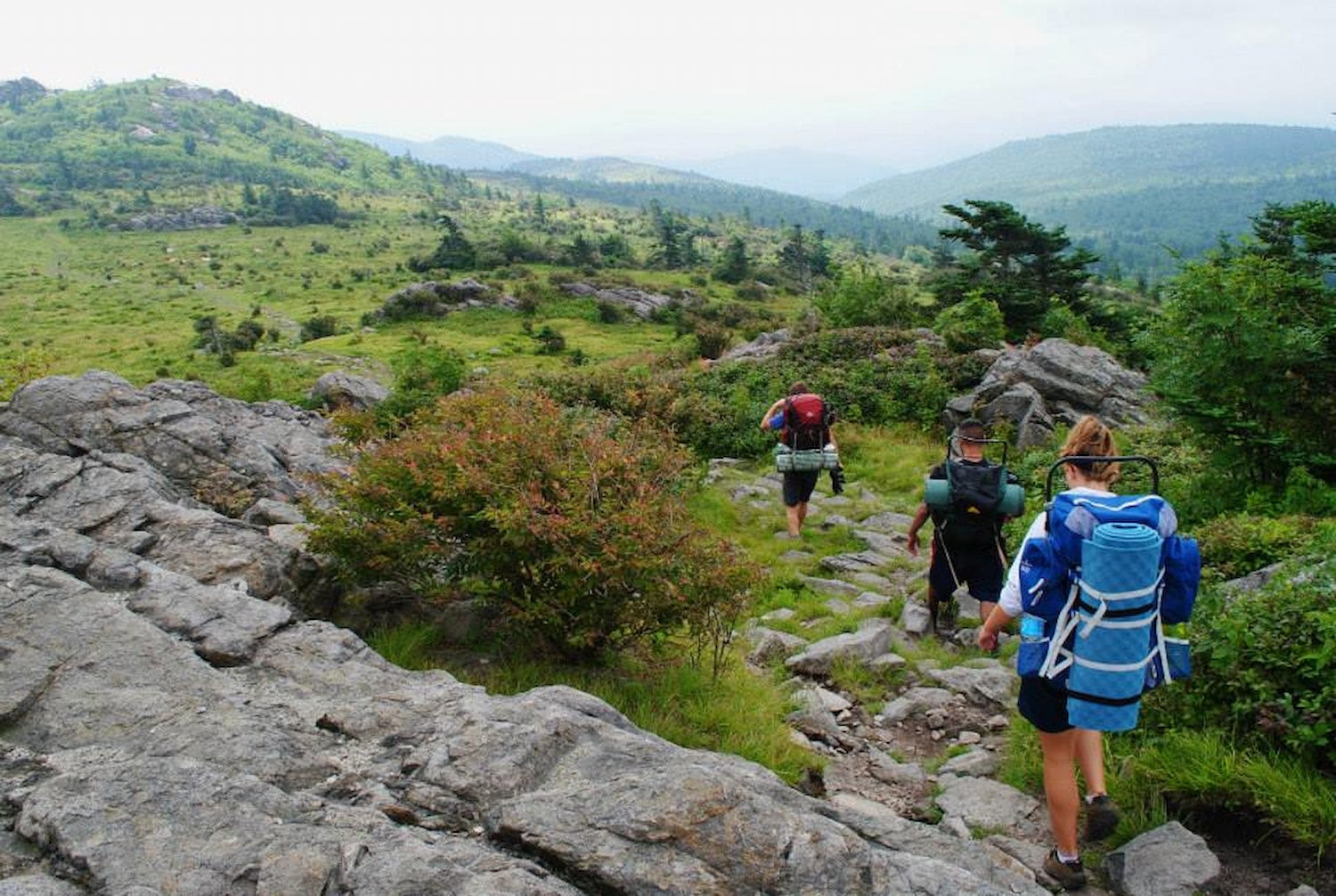 Backpackers hiking the rocky trails of Grayson Highlands surrounded by lush rolling hills.