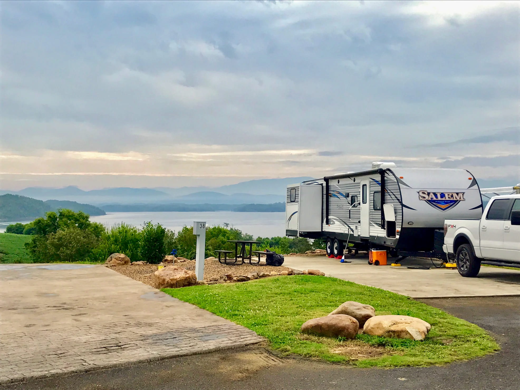 RV parked beside lake with mountains in the background.