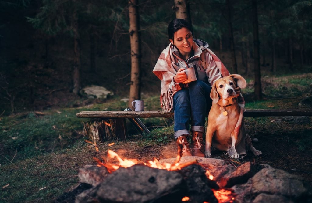 A camper with her dog by the fire.