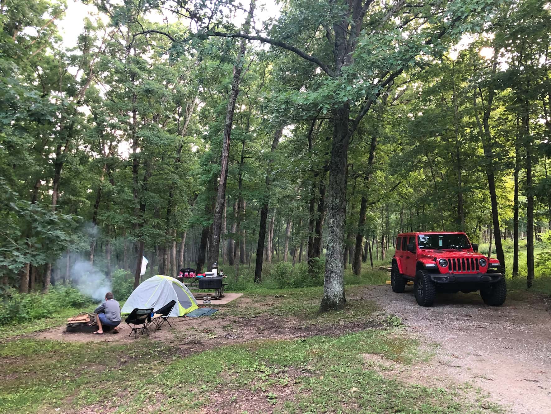 Jeep wrangler parked at campsite beside tent and campfire in the woods.