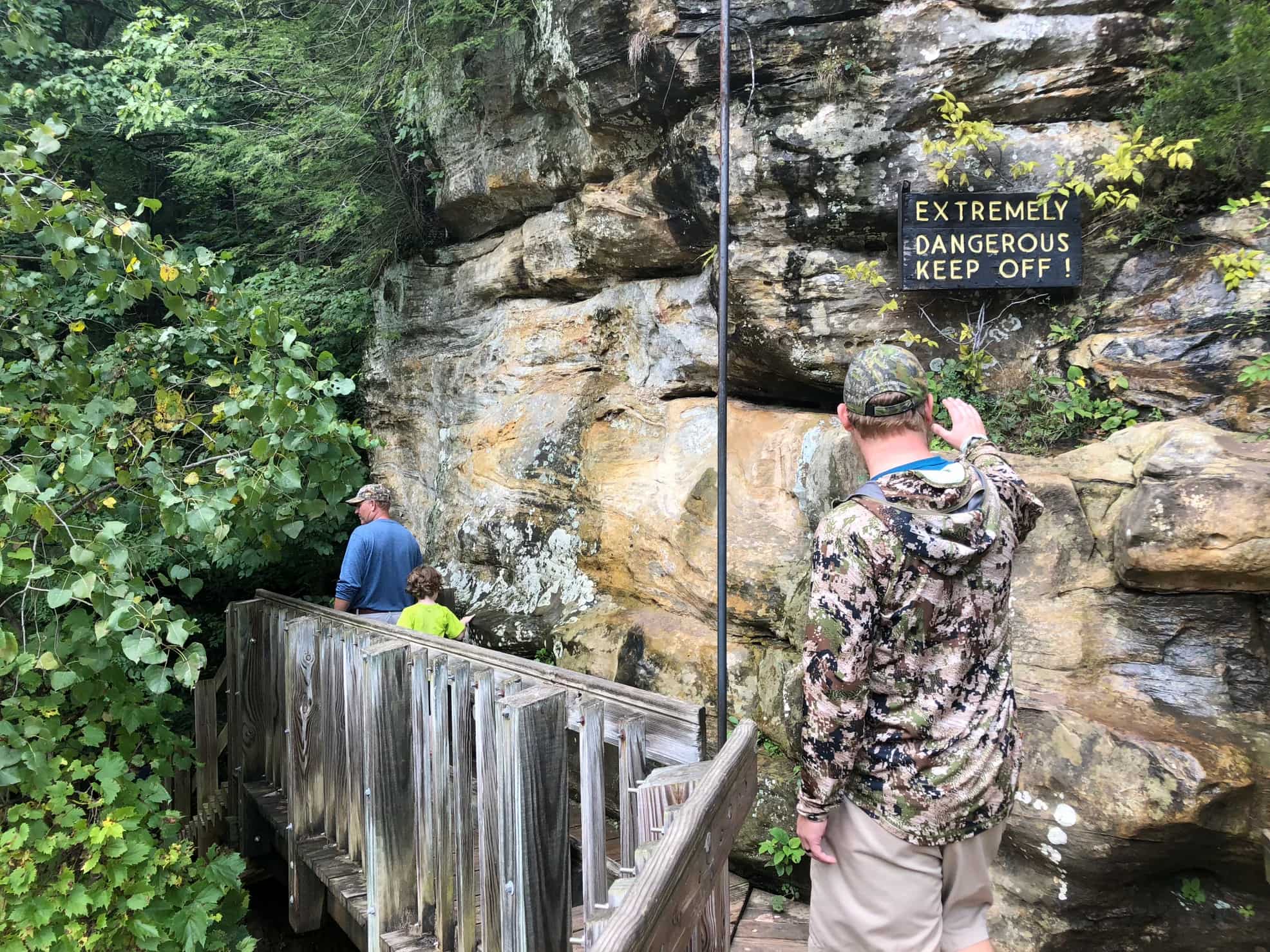 Park visitors walking along cave wall with wooden railing.