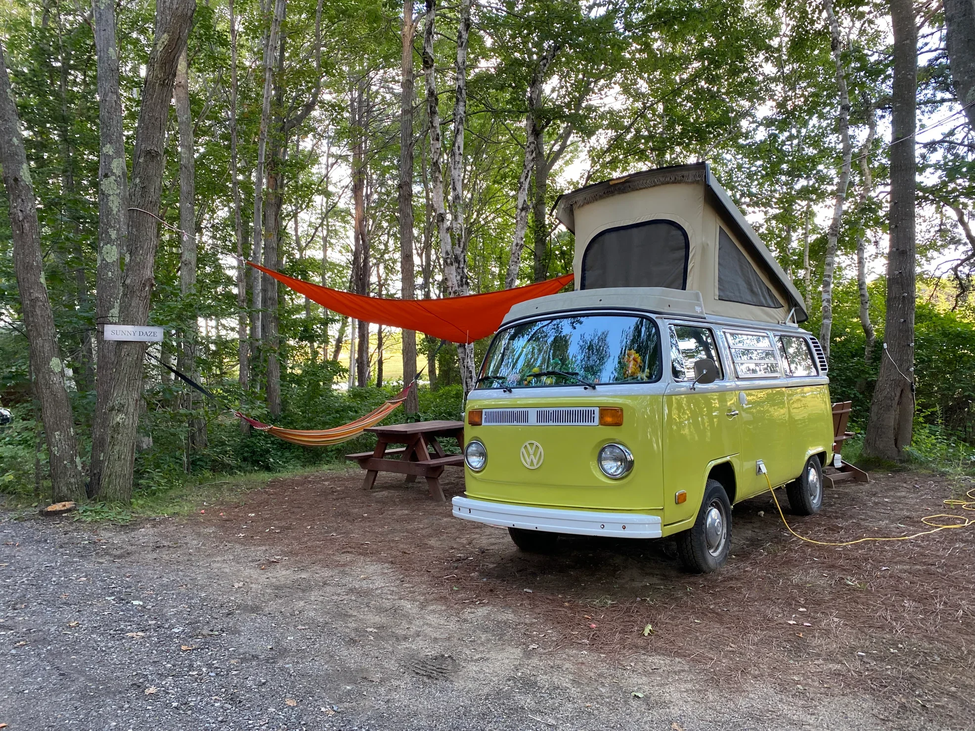 Lime green vintage westfalia parked at a cmapsite beside a hammock in the woods of Maine.