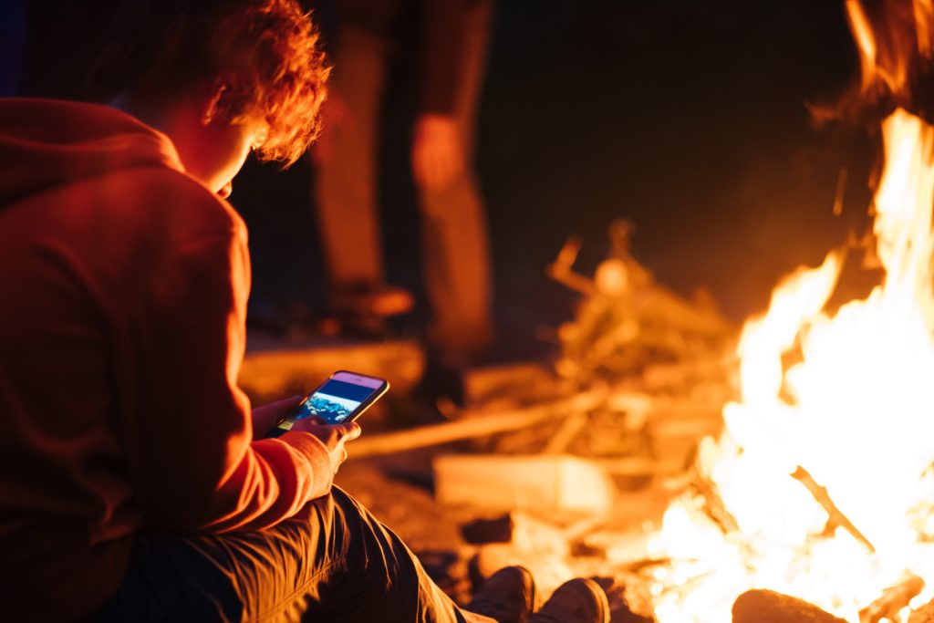 A Millennial by the campfire with a smartphone.