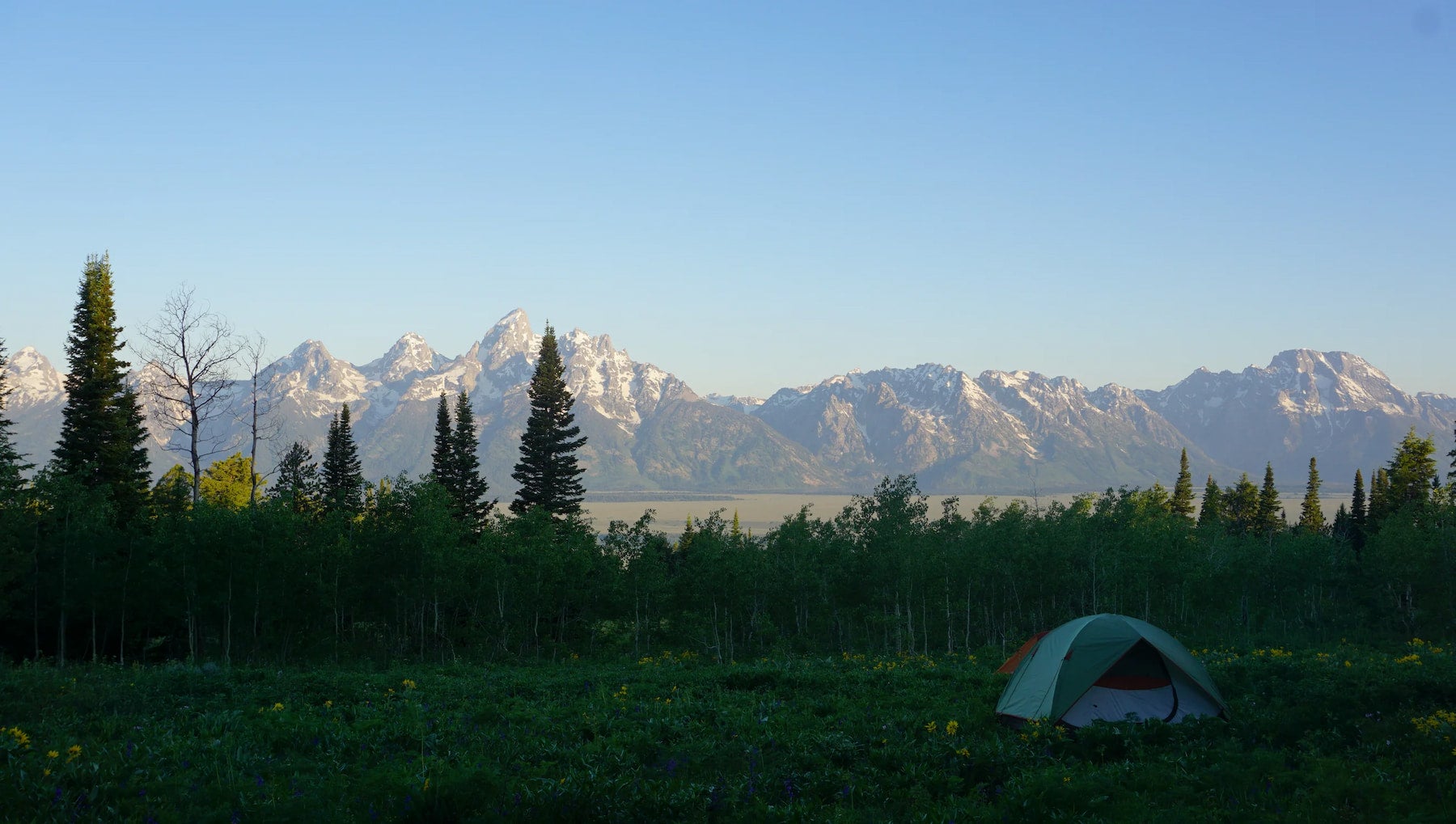 Tent pitched on field below a panoramic mountain landscape.