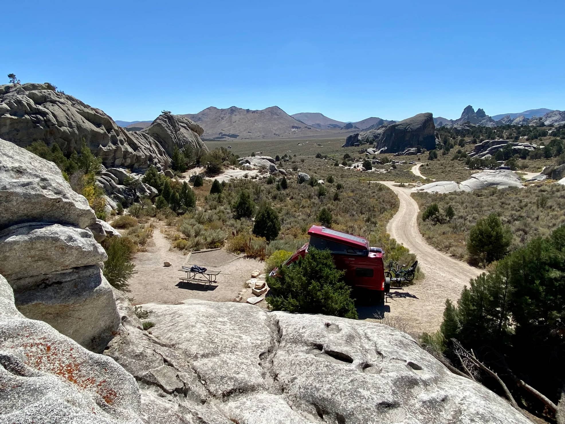 Red pop up camper van parked in campsite down a winding road surrounded by rock formations.