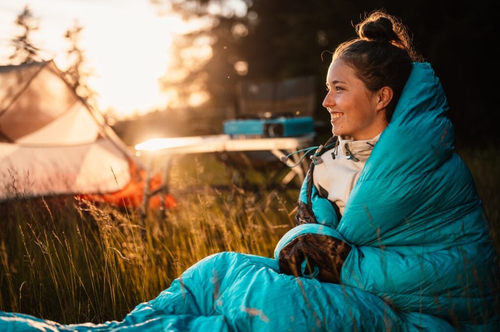 Woman in a sleeping bag staying warm on a cold morning tent camping.